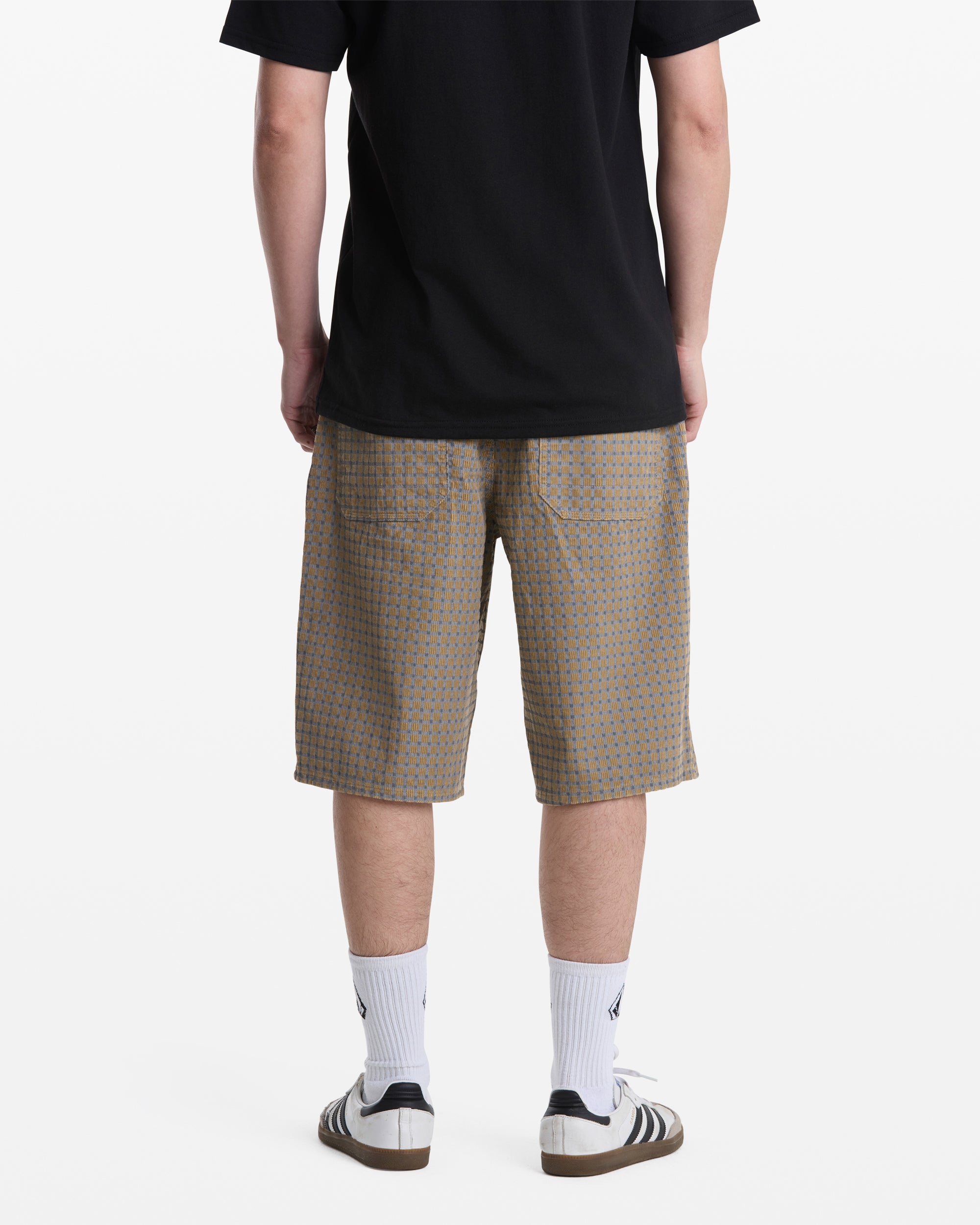 A person stands facing away against a plain white background, wearing Volcom Men's Chillow Shorts, a black t-shirt, white crew socks, and white sandals with dark soles.