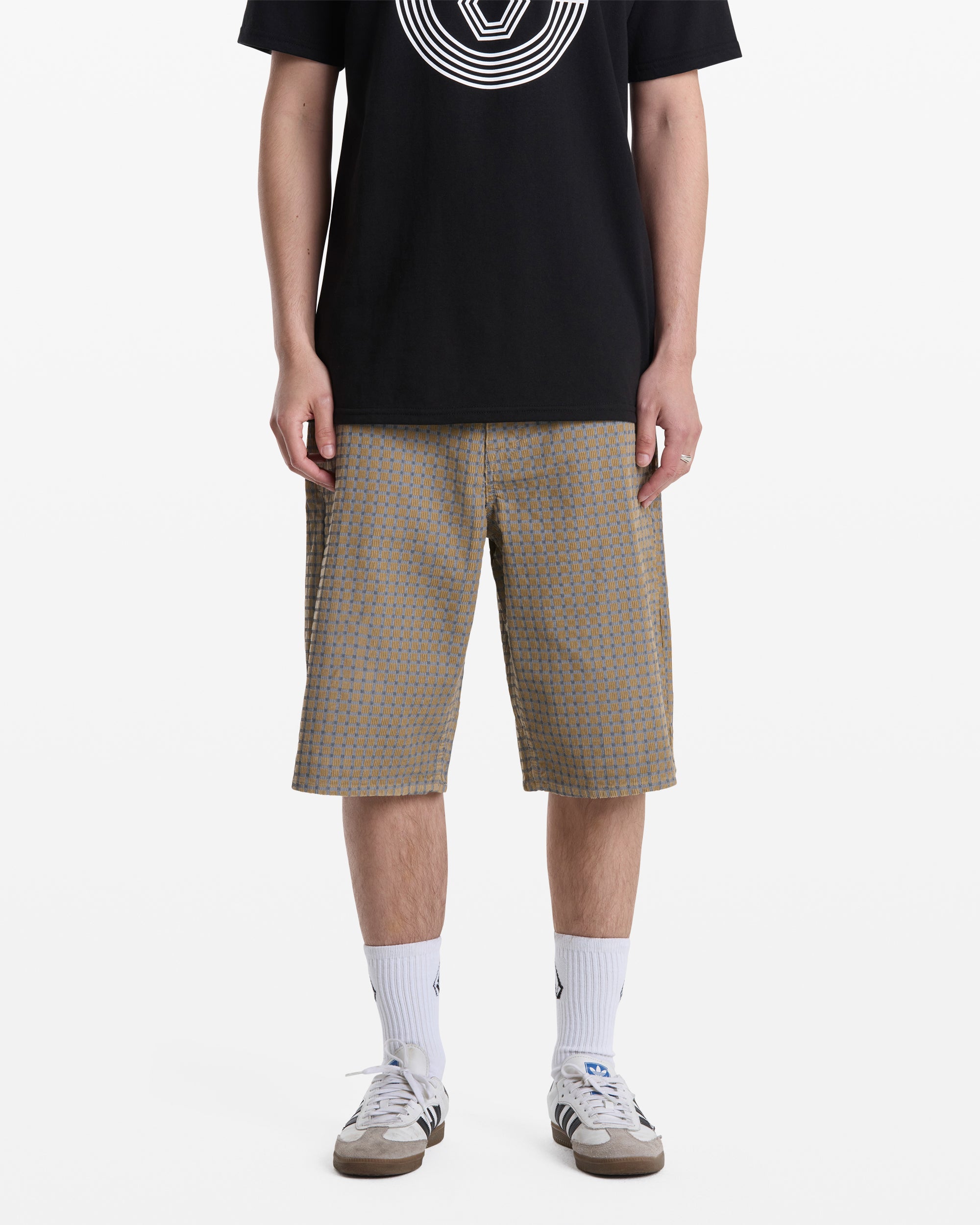 A person wearing Volcom Men's Chillow Shorts, a black T-shirt with a white circular design, white crew socks, and beige sneakers stands against a plain white background. Their face is not visible.