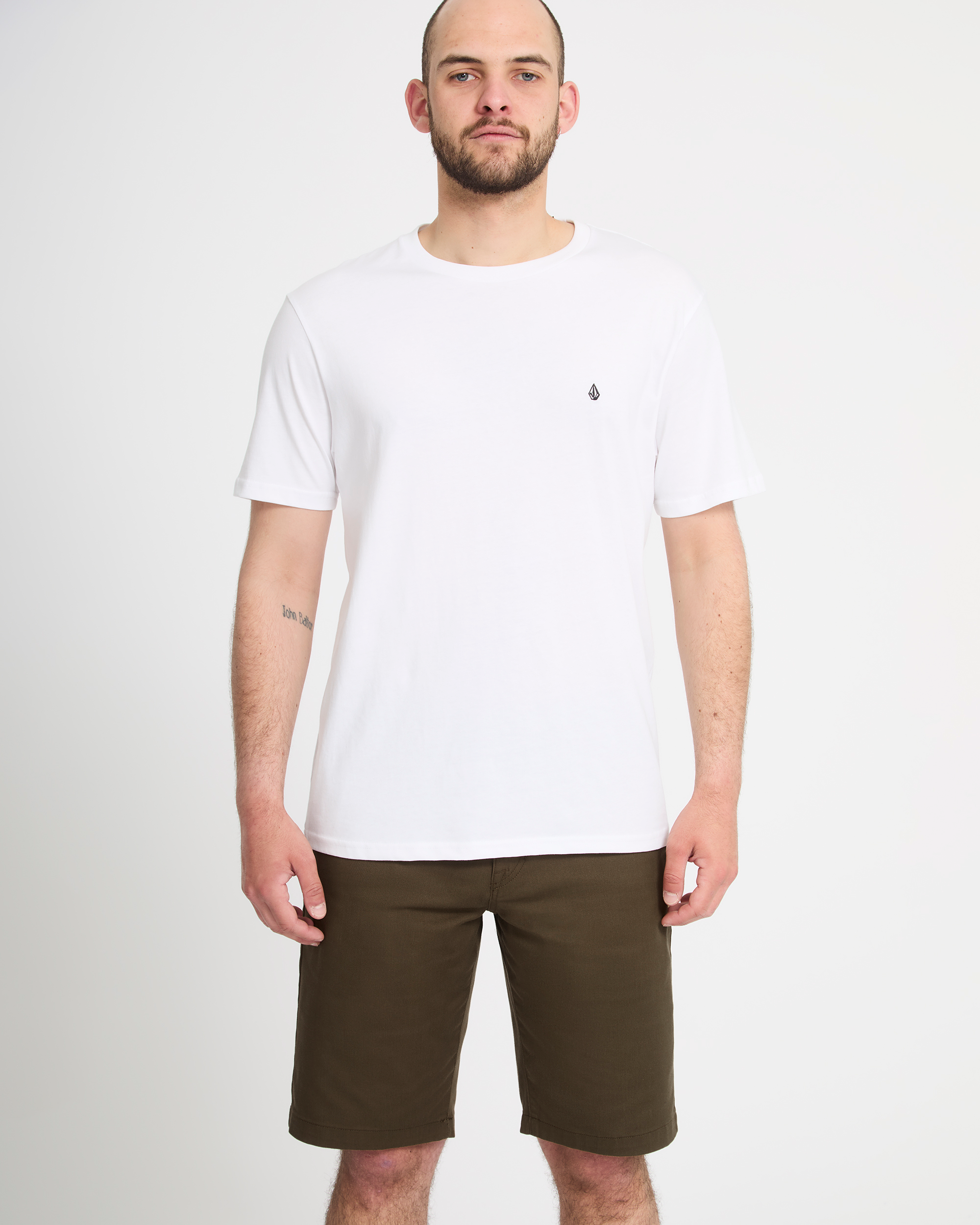 A man faces forward against a white background, wearing a plain white t-shirt and olive green Volcom Men's Frickin Modern Stretch Shorts.