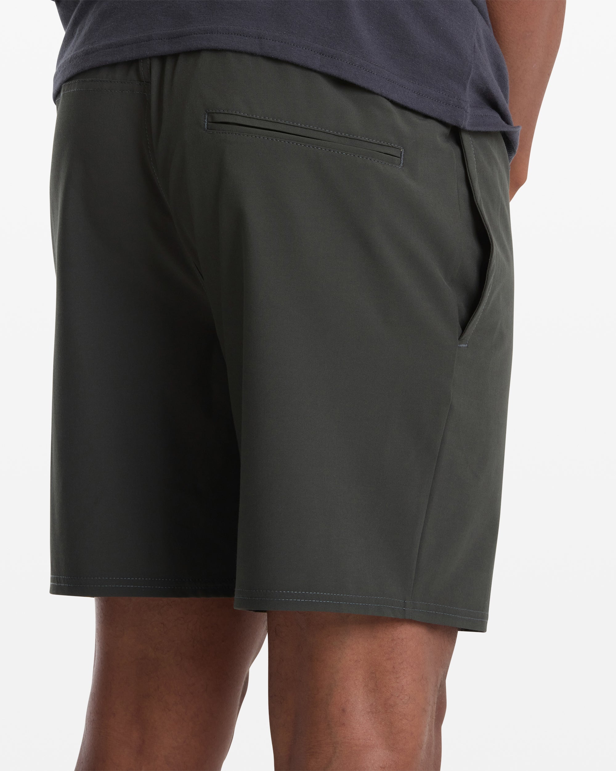 A person is seen from the back wearing Volcom Men's Nomoly Elastic Waist Short 18 in dark green, with one hand in the right pocket, featuring a back pocket and paired with a dark shirt.
