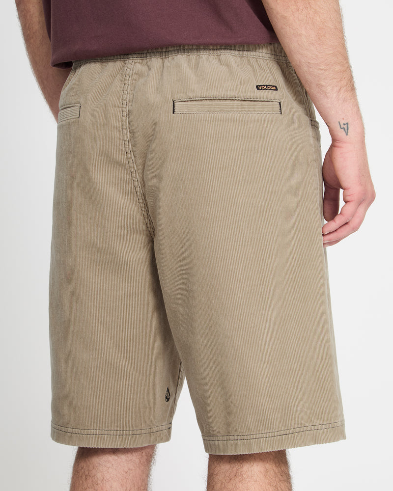 A person is shown from the back wearing Volcom Men's Freazy Loose Elastic Waist Short 22 in tan, featuring two back welt pockets, a small logo near the pocket, a maroon shirt, and a small forearm tattoo.