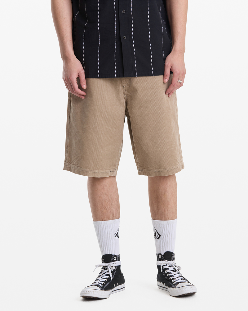 A person wears Volcom Men's Freazy Loose Elastic Waist Short 22 in beige, a black short-sleeved shirt with white stripes, white logo crew socks, and black low-top sneakers. The photo is cropped at the shoulders.