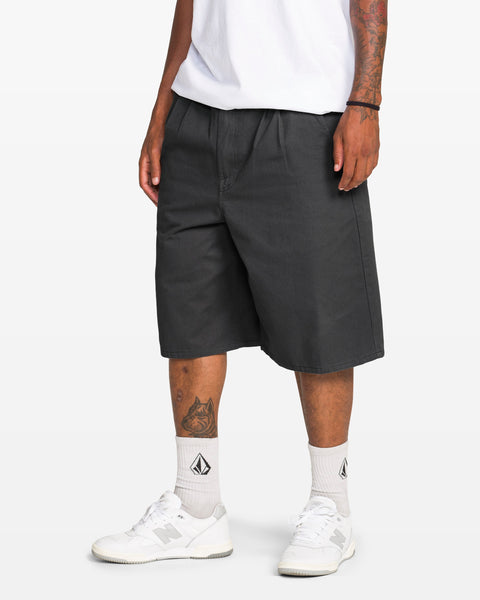 A person with tattooed arms and legs wears a white t-shirt, Volcom Men's Chillow Plt Elastic Waist Chino 24" Shorts Vs, white socks with a black logo, and white sneakers against a plain white background.