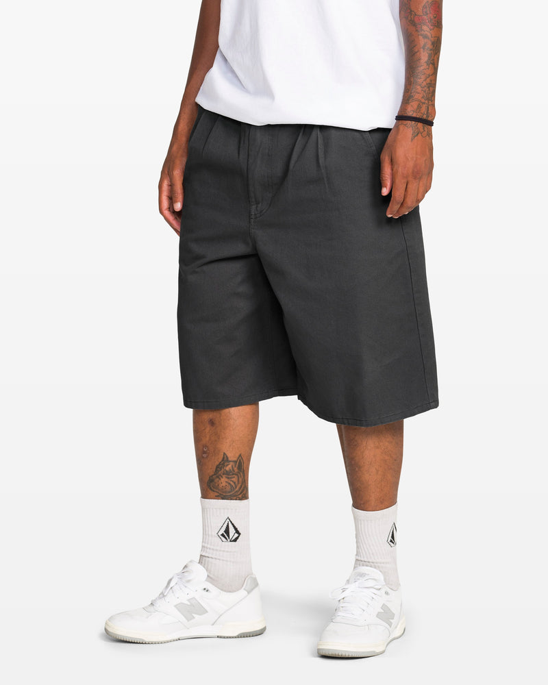 A person with tattooed arms and legs wears a white t-shirt, Volcom Men's Chillow Plt Elastic Waist Chino 24" Shorts Vs, white socks with a black logo, and white sneakers against a plain white background.