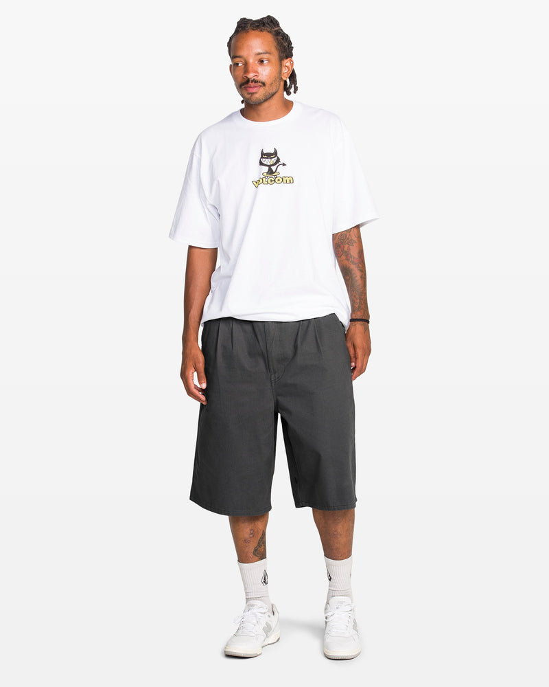 A man with braided hair wears a white graphic tee, Volcom Men's Chillow Plt Elastic Waist Chino 24" Shorts Vs in dark gray, white crew socks, and white sneakers, standing against a plain white background.