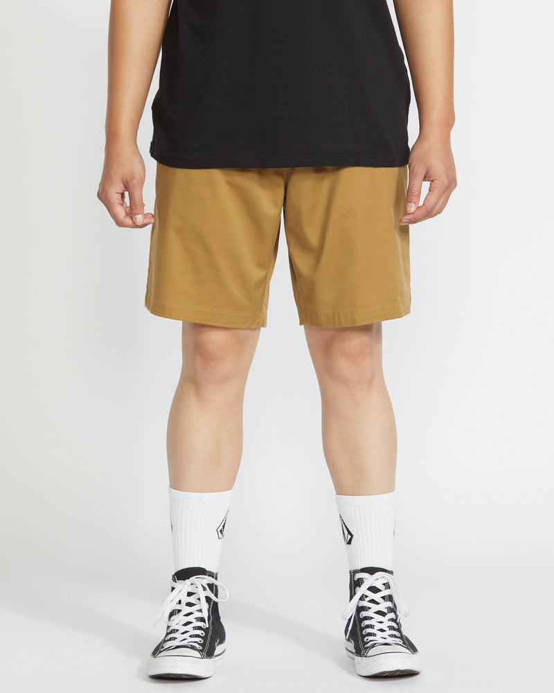 A person wears a black t-shirt, Volcom Men's Frickin Elastic Waist Shorts made with REPREVE fibers, white crew socks with a black logo, and black low-top sneakers, standing against a plain white background.