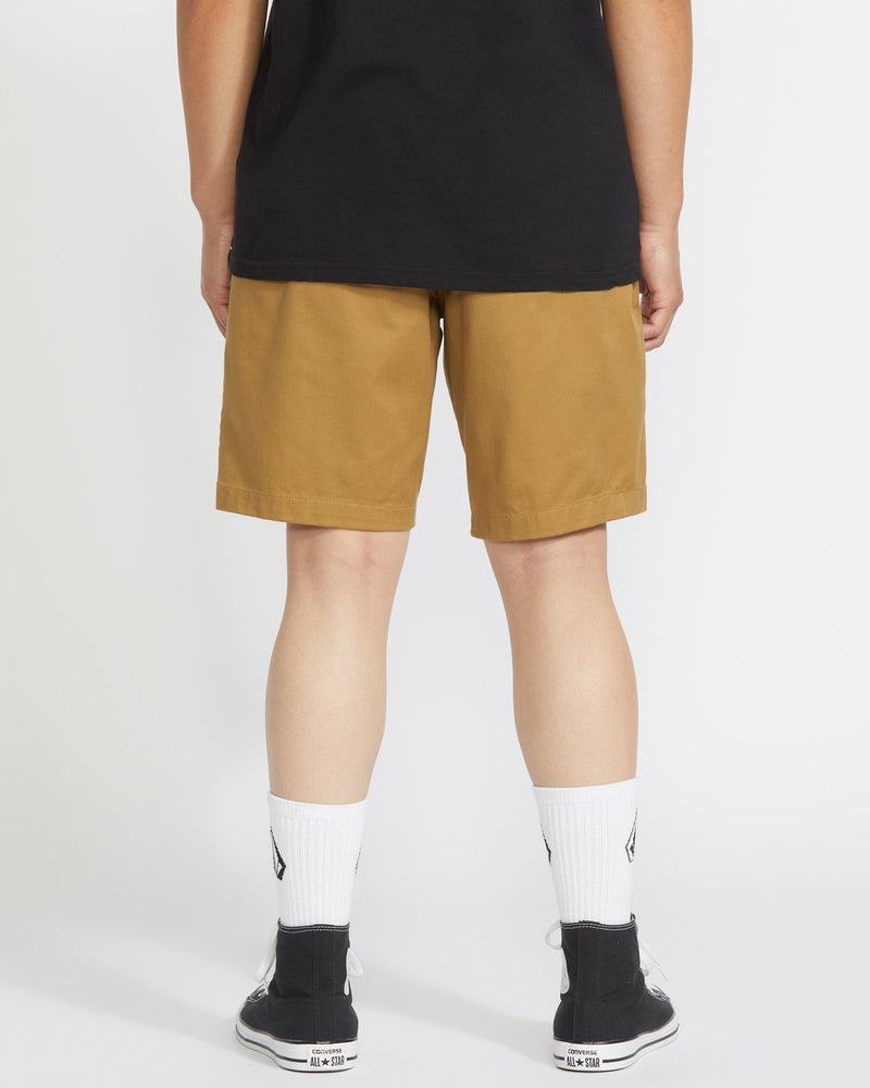 A person stands facing away from the camera wearing a black t-shirt, Volcom Men's Frickin Elastic Waist Shorts, white crew socks, and black sneakers against a plain white background.
