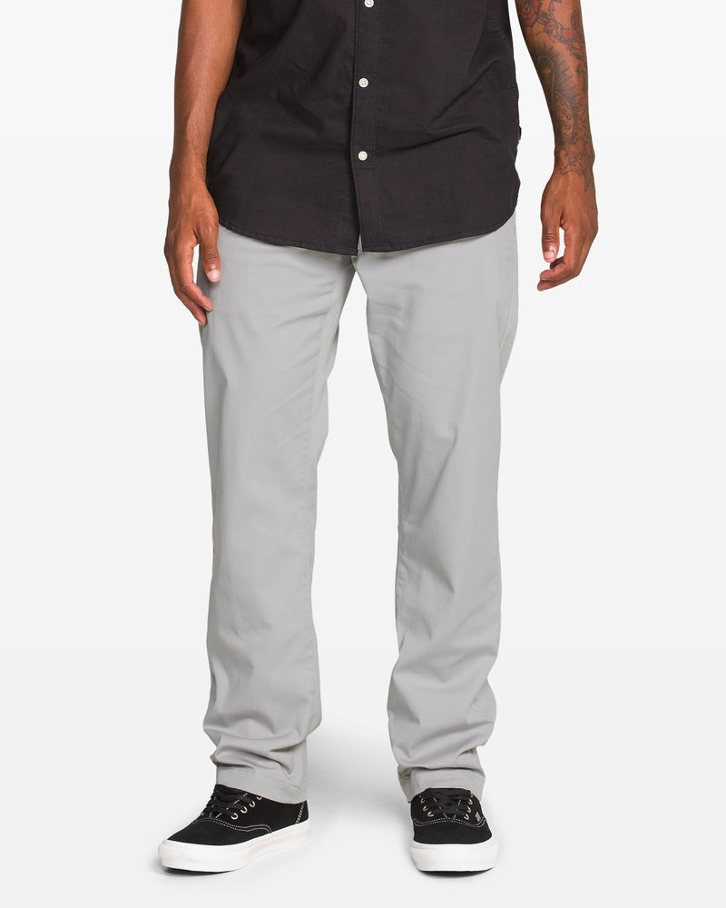 A person wearing a black short-sleeve button-up shirt, light gray pants, and black sneakers with white soles, standing against a plain white background.