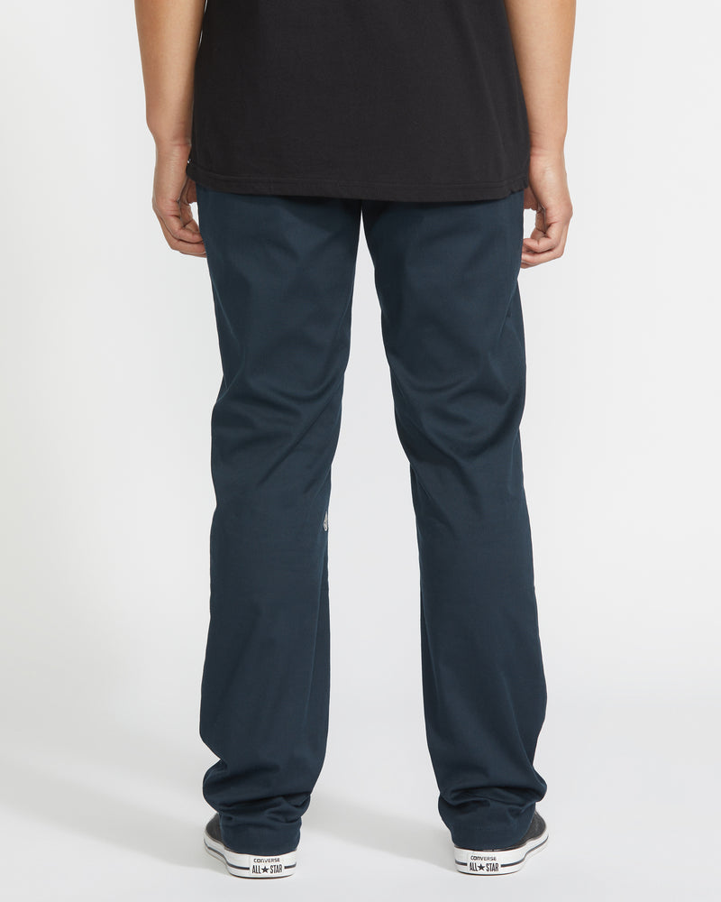 A person stands facing away from the camera, wearing a black shirt, white sneakers, and Volcom Men's Frickin Modern Stretch Pants (slim-fit, five-pocket) against a plain white background.