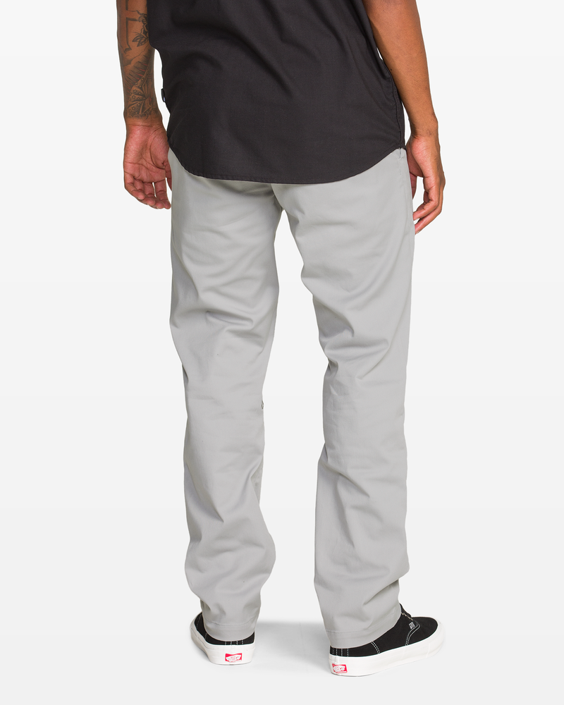 A man, seen from behind with only his lower half visible, wears Volcom Men's Frickin Modern Stretch Pants made from recycled polyester, paired with a black shirt and black-and-white sneakers.