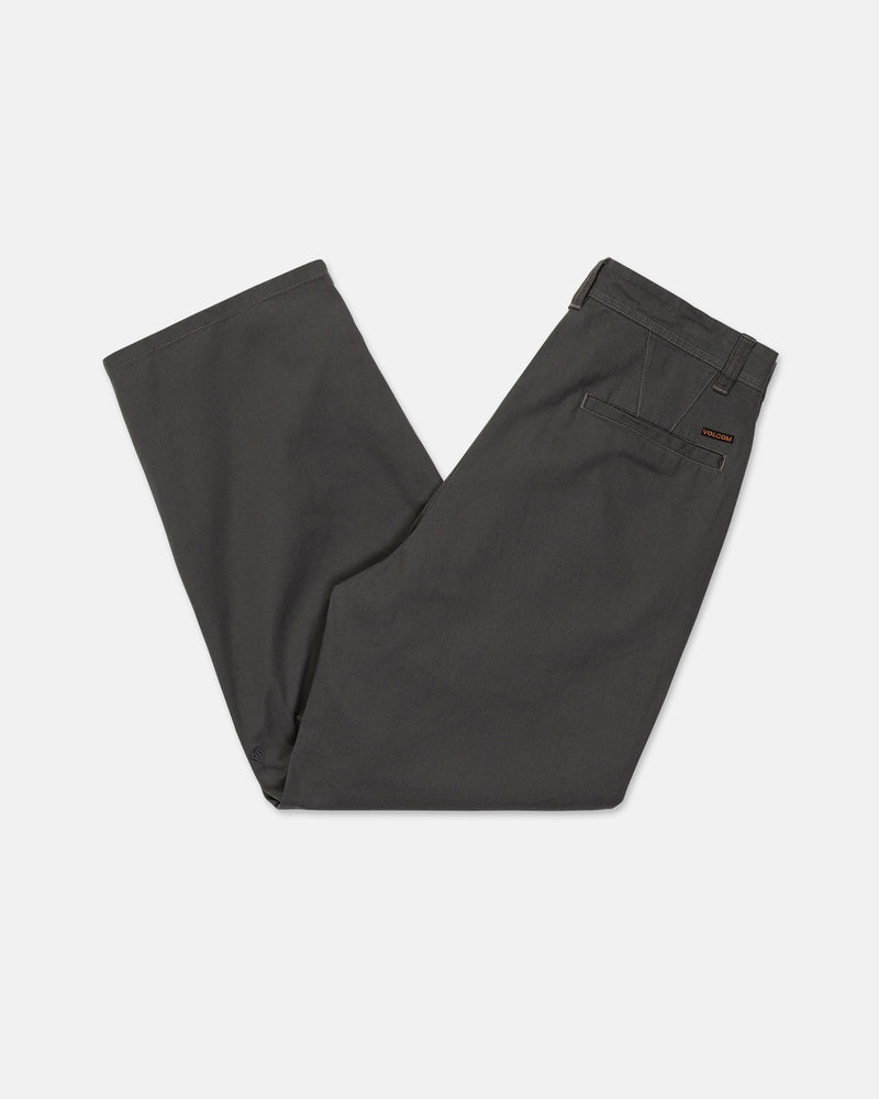 A pair of Men's Baggos Pleat Pants by Volcom in dark gray cotton, neatly folded in half with the waistband and back pocket visible against a white background.