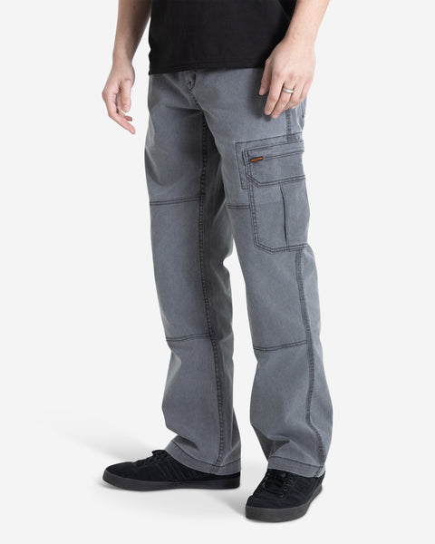 A person stands against a white background wearing Volcom Men's Gage Work Pants in gray, featuring visible stitching and a side cargo pocket, paired with black sneakers. The upper body is partially visible.