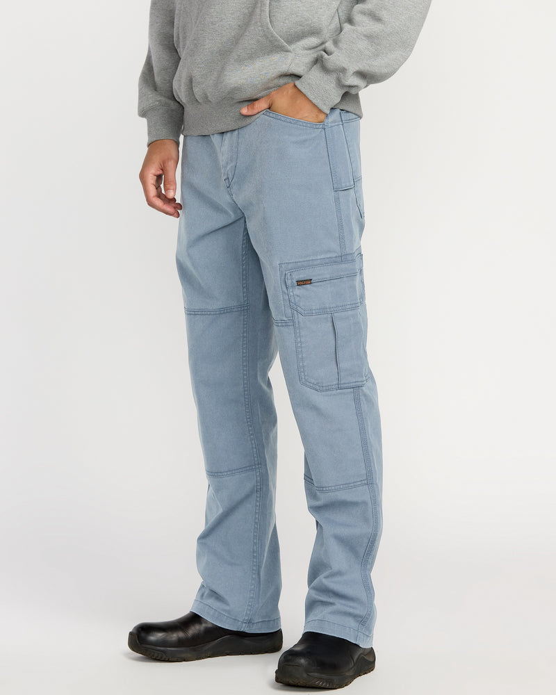 A person models Volcom Men’s Gage Work Pants in light blue, paired with a gray hoodie and black shoes against a white background. One hand is in their pocket, and their face is not shown.