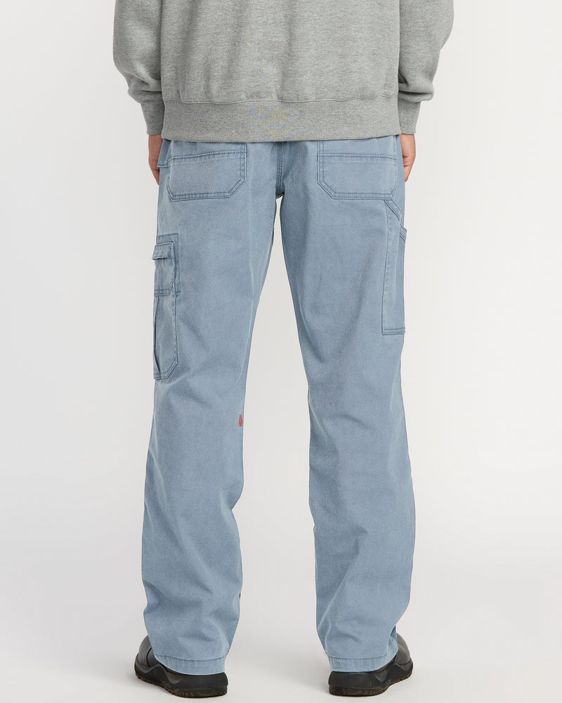 A person is shown from the back wearing Volcom Men's Gage Work Pants in light blue denim with large back and side pockets, paired with a gray sweatshirt, standing against a white background.