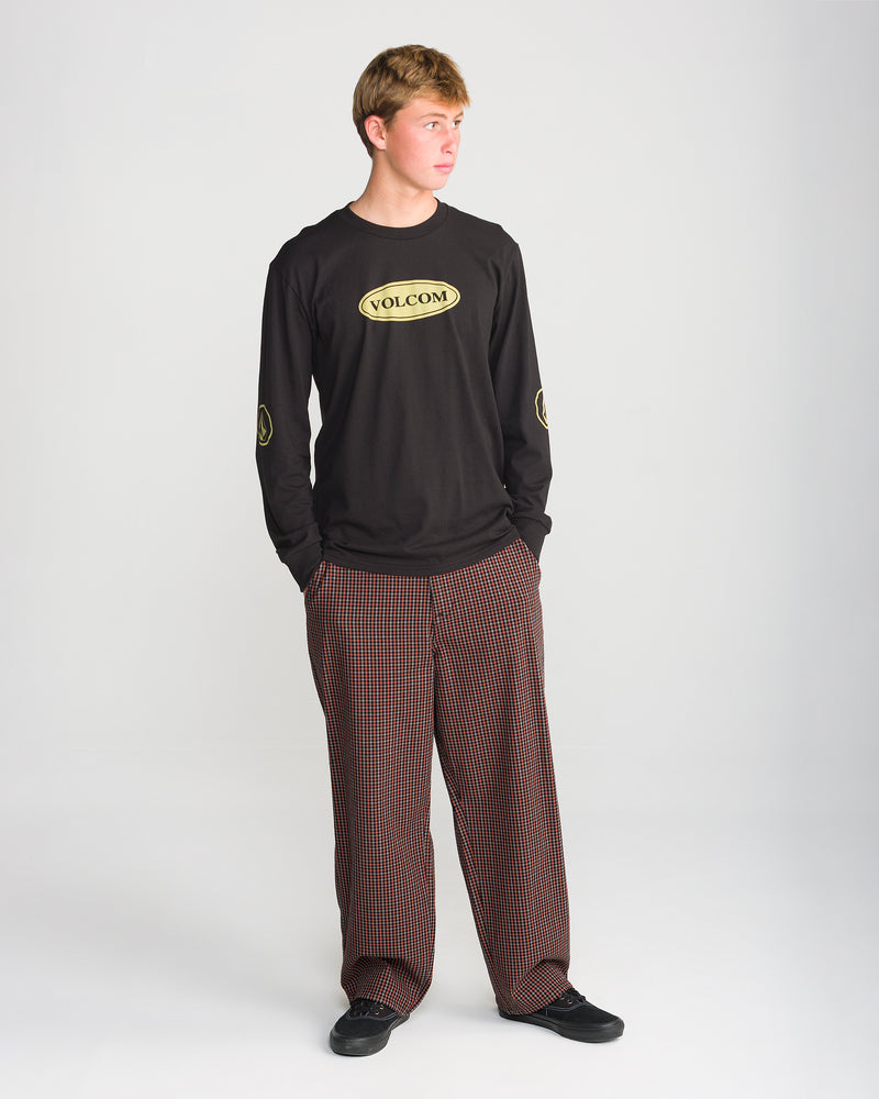 A person wearing a black long-sleeve shirt with yellow logos and Volcom Men’s Billow Plaid Pant in wide-leg red and black box plaid twill.