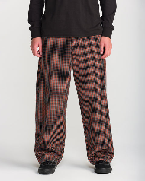 A person wearing Volcom Men’s Billow Plaid Pant in loose-fitting, brown and black box plaid twill with black sneakers.