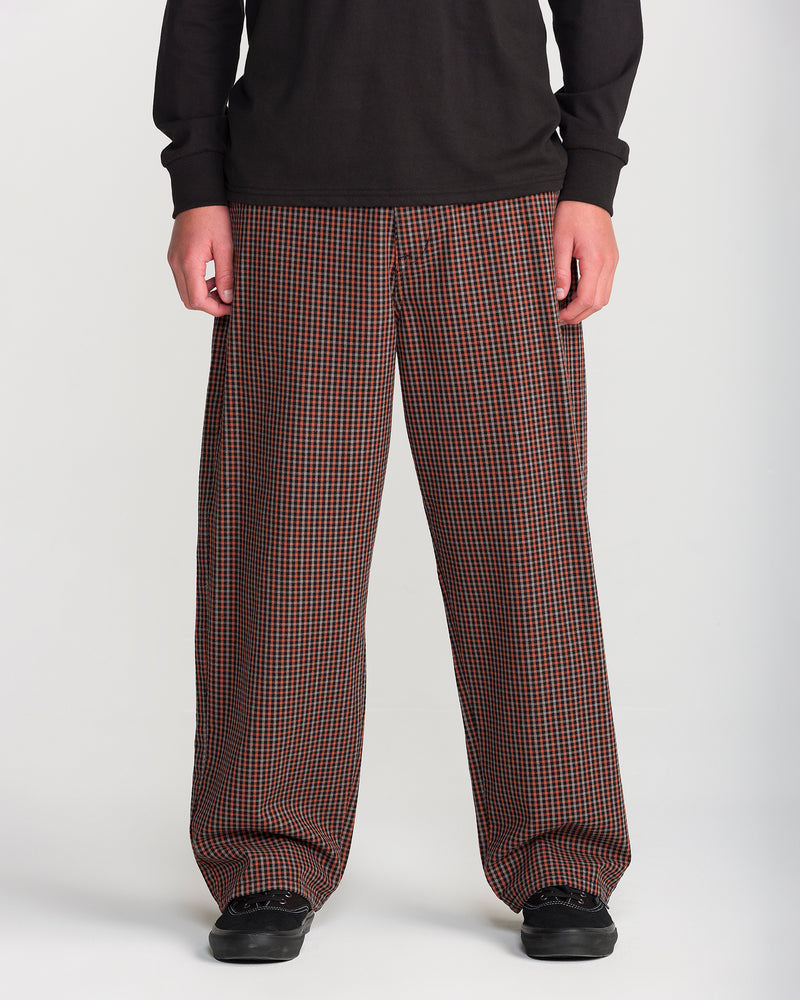 A person wearing Volcom Men’s Billow Plaid Pant in loose-fitting, brown and black box plaid twill with black sneakers.