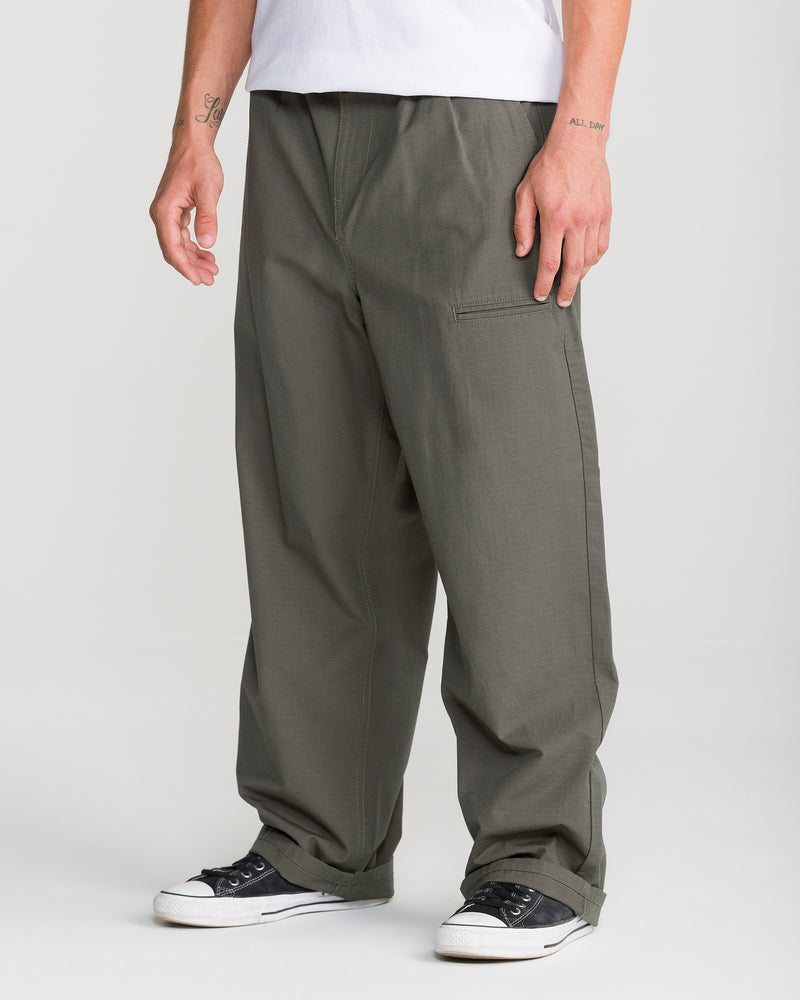 A person wears Volcom Men’s Skuds Pant in olive green cotton ripstop with black and white sneakers and a white shirt, showing only the lower half against a plain light background.
