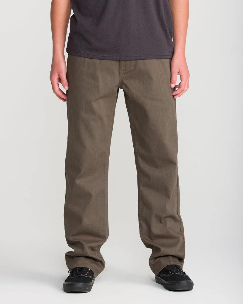 A person wearing a dark t-shirt, Men’s Kinkade Slub Pant by Volcom with a straight leg, and black shoes stands against a plain white background.