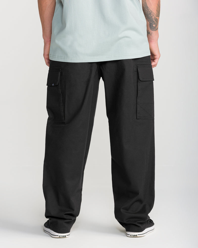 A person is shown from the waist down, wearing Volcom’s Men’s Billow Tapered Elastic Waist Cargo pants in black paired with a light-colored shirt, standing with their back to the camera.