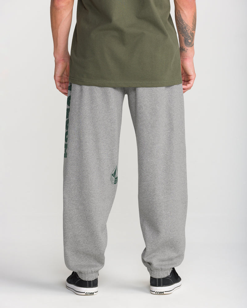 A person stands facing away in a green shirt, Men’s Quadratic Fleece Pant by Volcom (classic fit, small logo), and black sneakers against a plain white background.