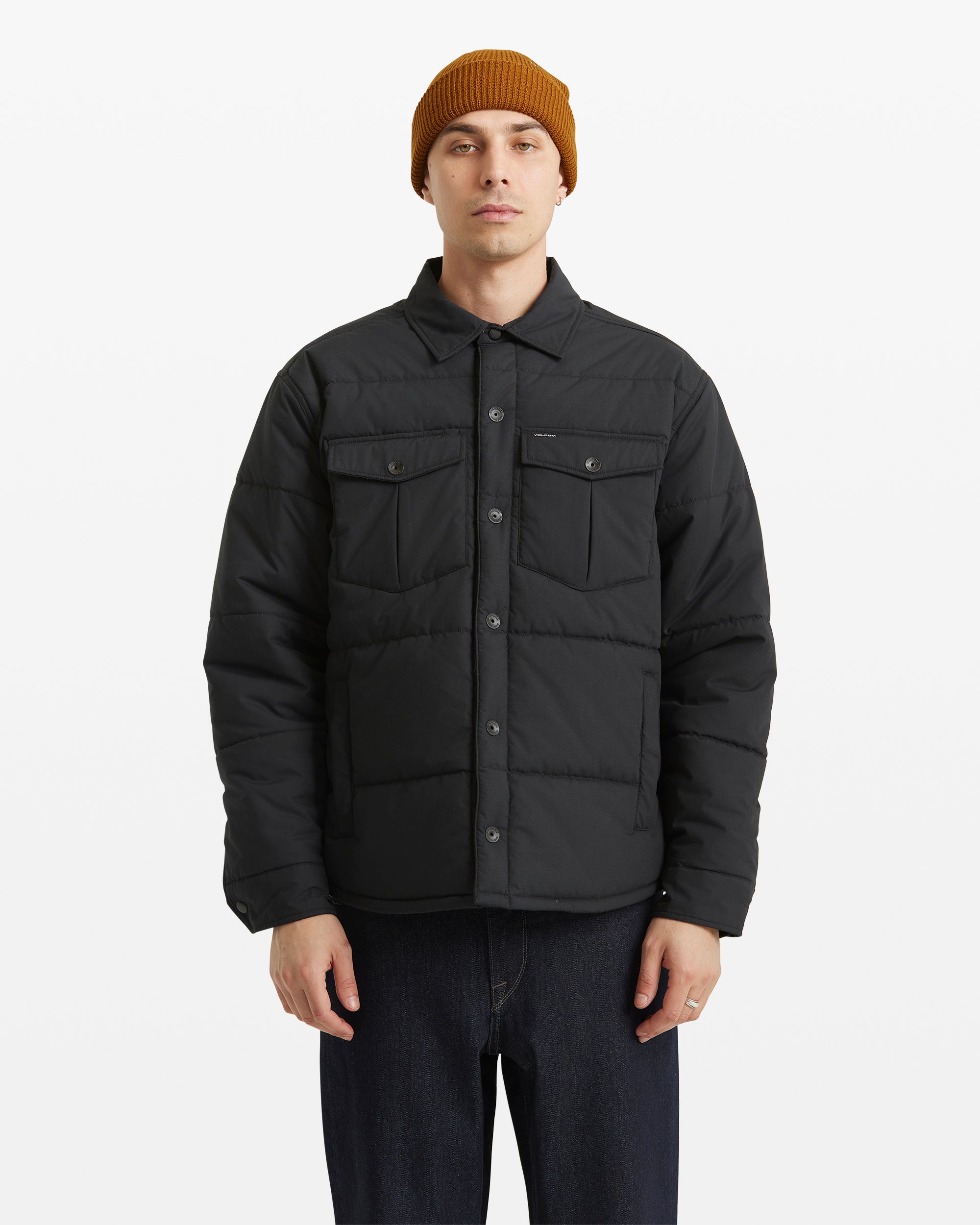 A person wearing a mustard beanie, dark jeans, and the Volcom Men's Westmead Quilted Jacket with buttoned chest pockets stands facing forward against a plain white background.