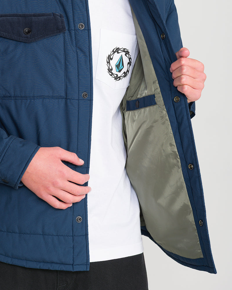 A person opening the front of a blue quilted Volcom Men’s Westshore Jacket to show the interior lining and a white t-shirt underneath.