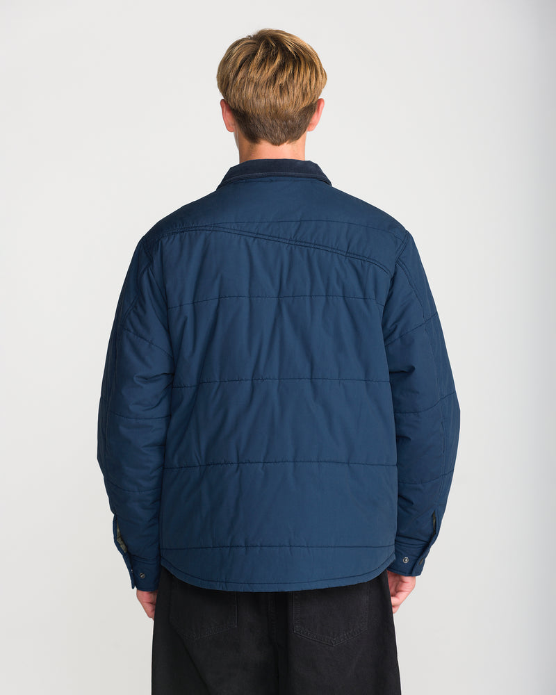 Back view of a person wearing a dark blue Volcom Men’s Westshore Jacket, a quilted shirt jacket with a corduroy collar.