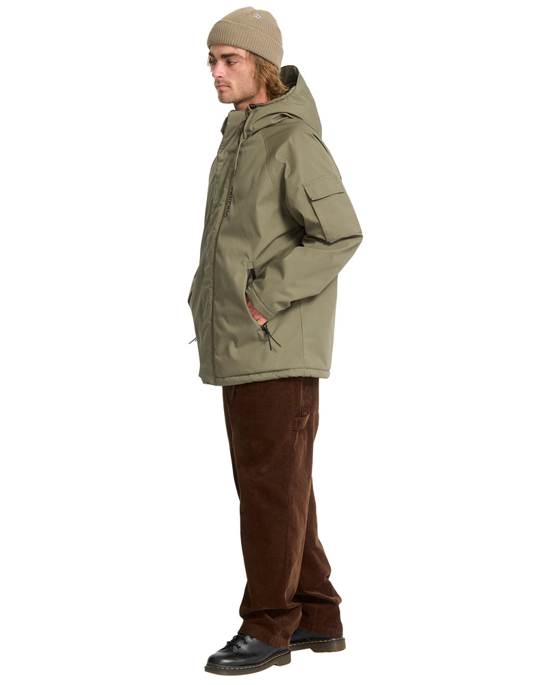 A man wears an olive green Volcom Men’s Stoke Stone II 10K Jacket with a hood and chest pocket, paired with brown corduroy pants and a beanie.