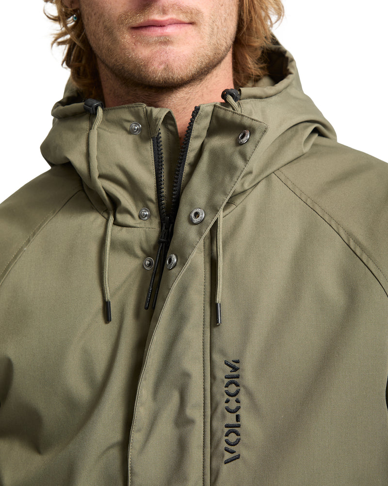 A man wearing a Volcom Men’s Stoke Stone II 10K Jacket, an olive green water-resistant hooded jacket with a full front zipper, snap buttons, and a vertical logo embroidered on the chest.