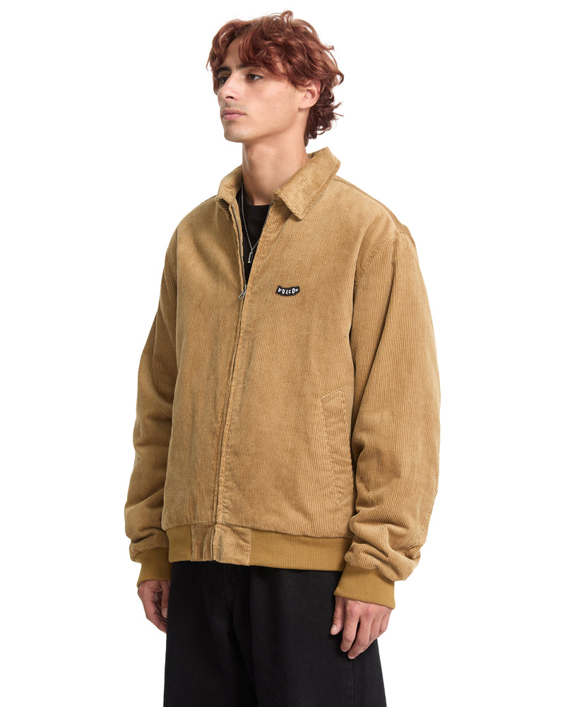 A person wearing a tan cotton corduroy Men’s Kurtis Jacket by Volcom, featuring a blouson fit with a ribbed hem and cuffs.