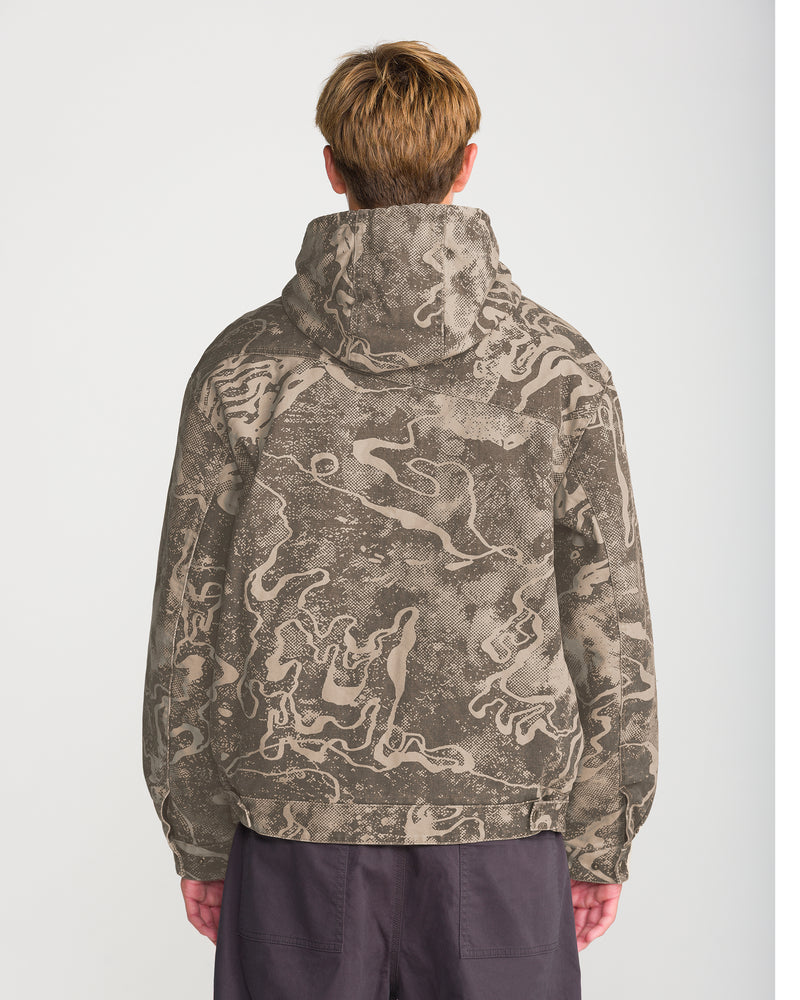 A person viewed from behind wears a Volcom Men’s Fresh Storm Workwear Jacket in a duck canvas hooded design with an abstract, tan-and-brown camo pattern.
