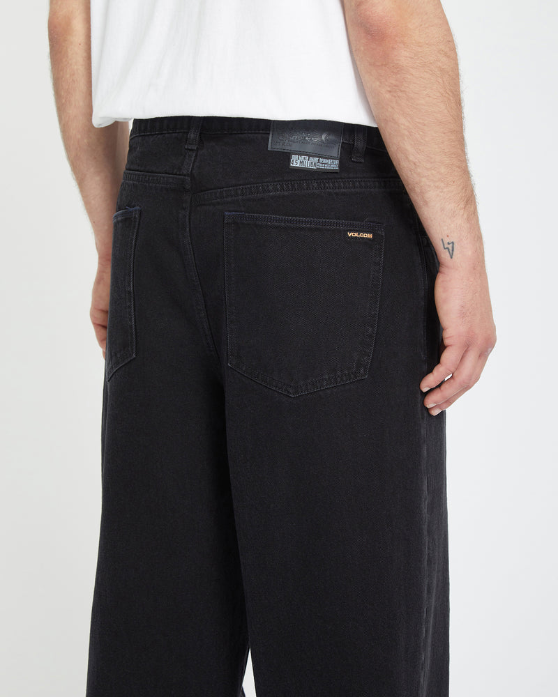 A person wearing a white T-shirt and baggy fit black Men's Chillow Denim jeans is shown from the back. The jeans have a visible patch above the pocket and a small VOLCOM logo on the right back pocket.
