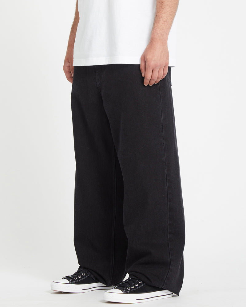 A person is seen from the shoulders down wearing a white T-shirt, black Men's Chillow Denim jeans with a baggy fit, and black-and-white sneakers against a plain white background.