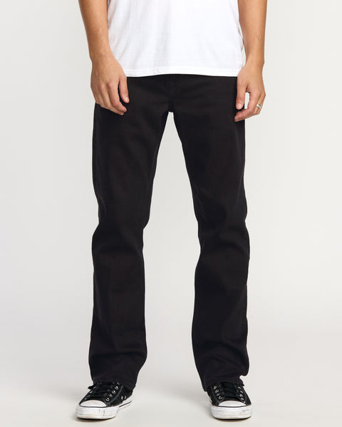 A person stands against a plain light background wearing a white T-shirt, black-and-white sneakers, and Volcom Men's Volcom Entertainment Pennywise Denim Pants. The image is cropped to show the body from shoulders down.