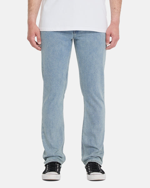 A person wearing Volcom Men's Vorta Denim Pants in light blue straight-leg style, paired with a white shirt and black sneakers, stands facing forward against a plain white background.