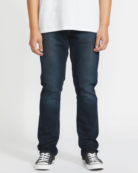 Wearing Volcom's Men's Vorta Denim jeans, a person stands against a plain white background. The image is cropped from the shoulders down and also shows a white t-shirt and black-and-white sneakers.