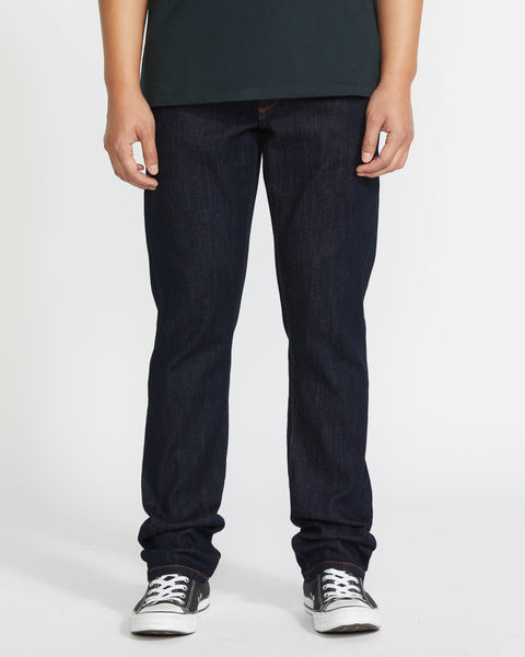 A person in a dark green T-shirt, Volcom Men's Vorta Denim slim fit jeans, and black-and-white sneakers stands against a plain white background. Their face is not visible.