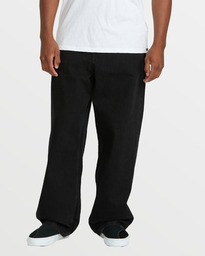 A person stands against a plain light background, wearing Volcom Men's Billow Denim jeans that resemble high-ridge twill, a white T-shirt, and black slip-on shoes with white soles. The image is cropped at the shoulders.