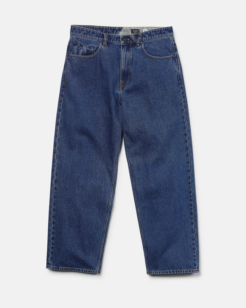 The Men's Billow Denim Pants by Volcom are a pair of loose fit, low rise jeans in a rich dark indigo wash, featuring a classic five-pocket design, button closure, and straight legs, shown laid flat on a white background.
