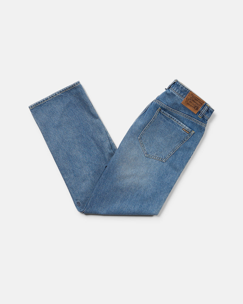 A pair of blue Men’s Pipe Dreams Denim Pants by Volcom, vintage-inspired and neatly folded with the back pocket and brown leather patch visible, displayed on a white background. These jeans feature a relaxed straight fit for timeless style and comfort.
