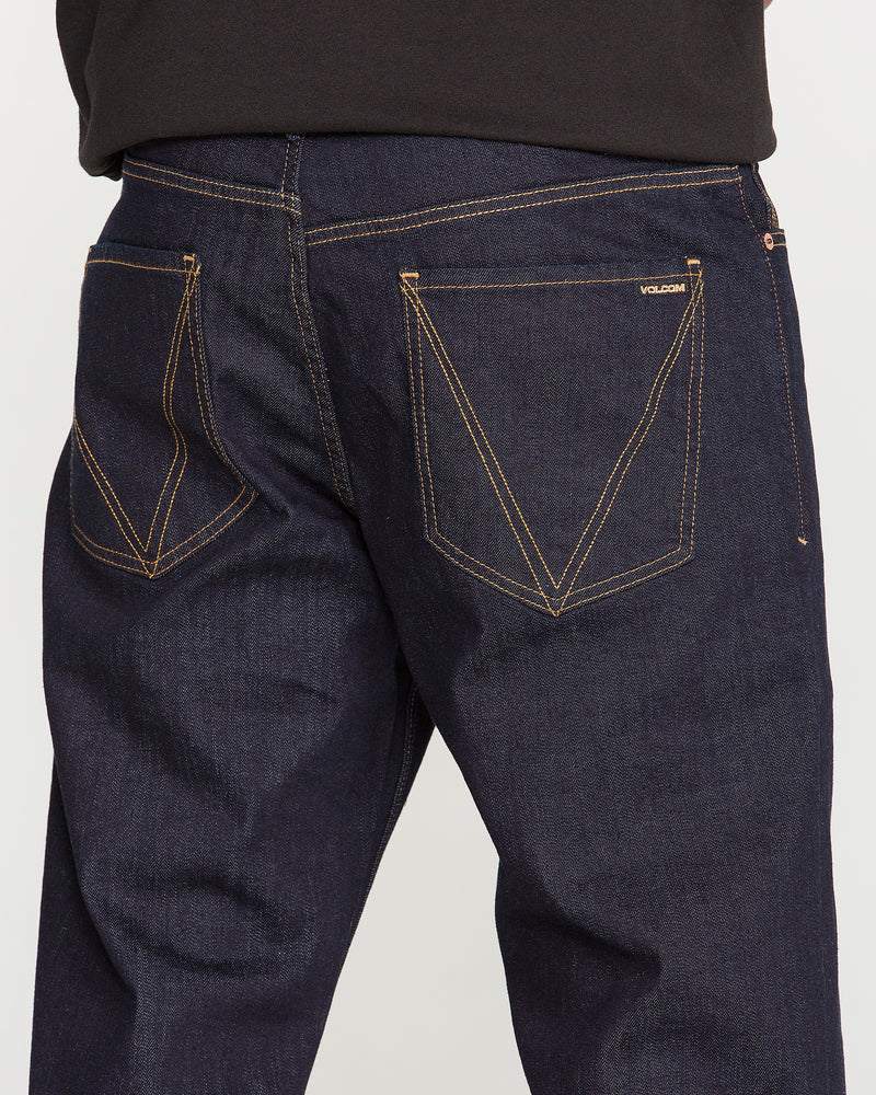 Close-up of the back of a person wearing Volcom Men's Pipe Dreams Denim Pants in dark blue indigo stretch denim, featuring contrasting orange stitching and two back pockets—one adorned with a small “Volcom” label that showcases the brand's signature details.