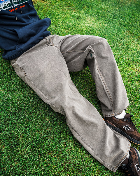 A person wearing Volcom Men’s Featured Artist Antonio Carrau Reverb Pants is sitting on green grass, with only their lower body visible.