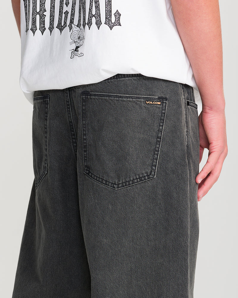 Person wearing a white graphic tee and loose fit Men’s Billow Denim by Volcom, shown from the back waist down. Jeans feature a small Volcom tag on the pocket; tee displays cartoon with ORIGINAL.