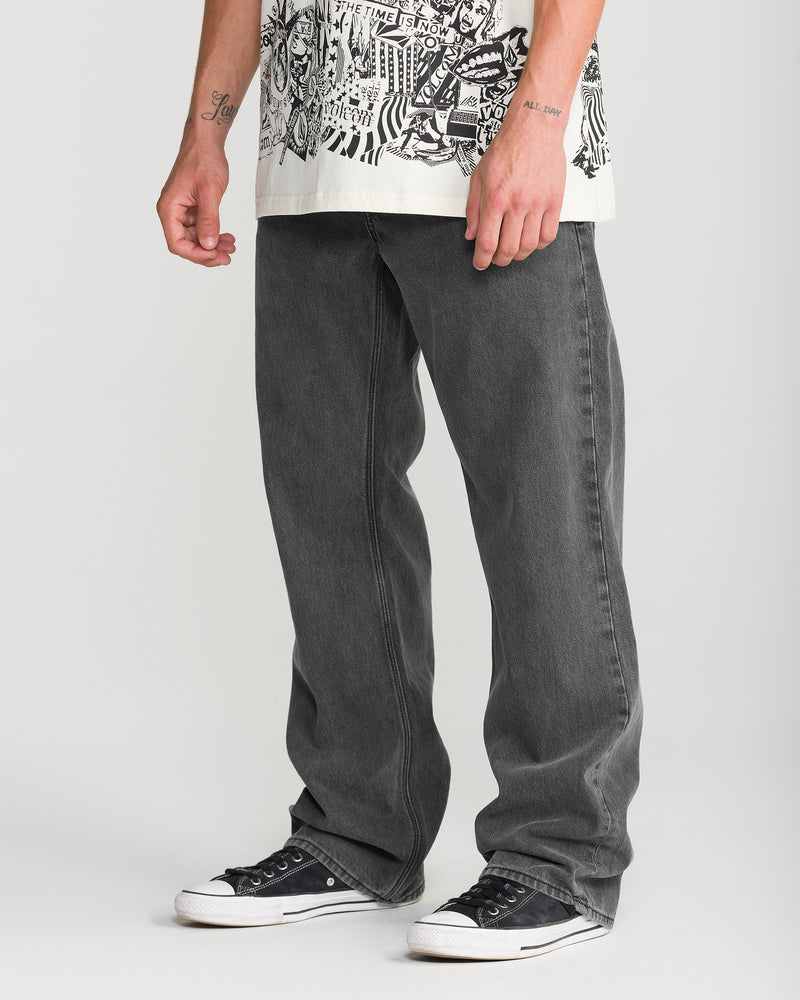 Person wearing relaxed straight fit charcoal grey Volcom Men’s Pipe Dreams Denim jeans and black sneakers.