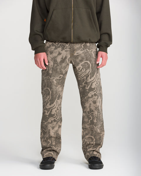 A person wears Volcom Men’s Kinkade Utility Denim and a dark green zip-up hoodie, standing facing forward with hands at their sides; only the lower half of their body is visible.