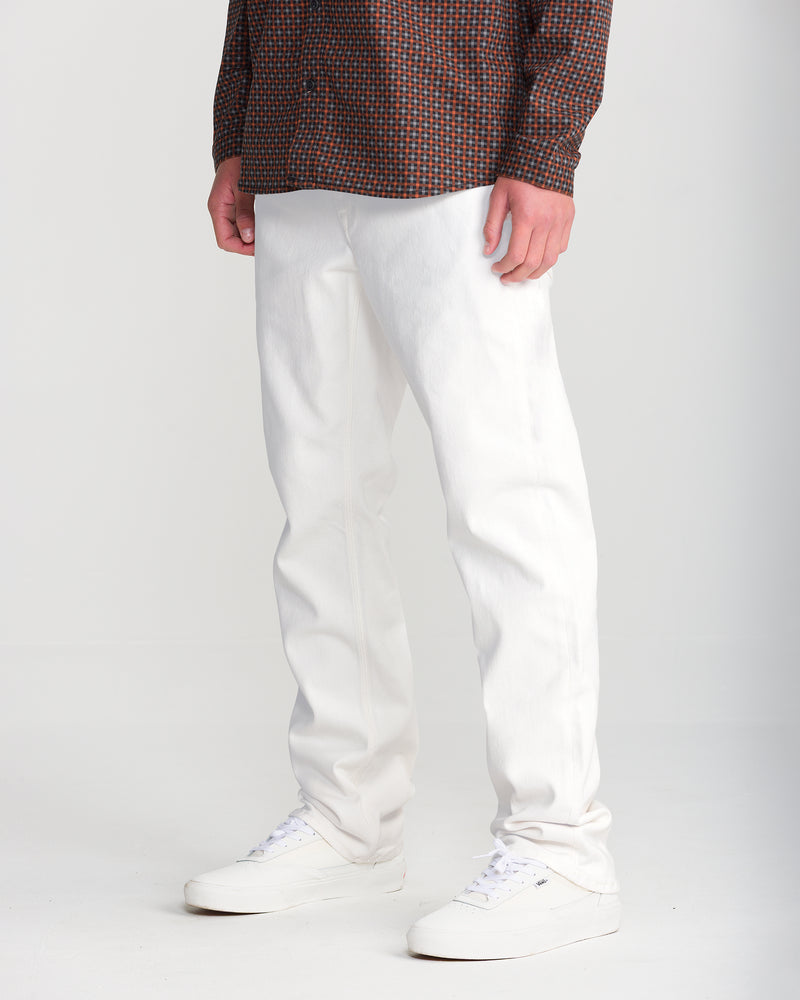 A person wearing Volcom Men’s Solver Denim in white, a plaid button-down shirt, and white sneakers.