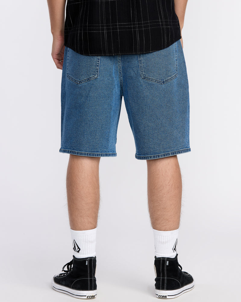 A person is shown from the back wearing Volcom Men's Billow Denim Shorts, a black shirt, white socks, and black sneakers against a plain white background. The shorts feature eco-friendly Water Aware construction.