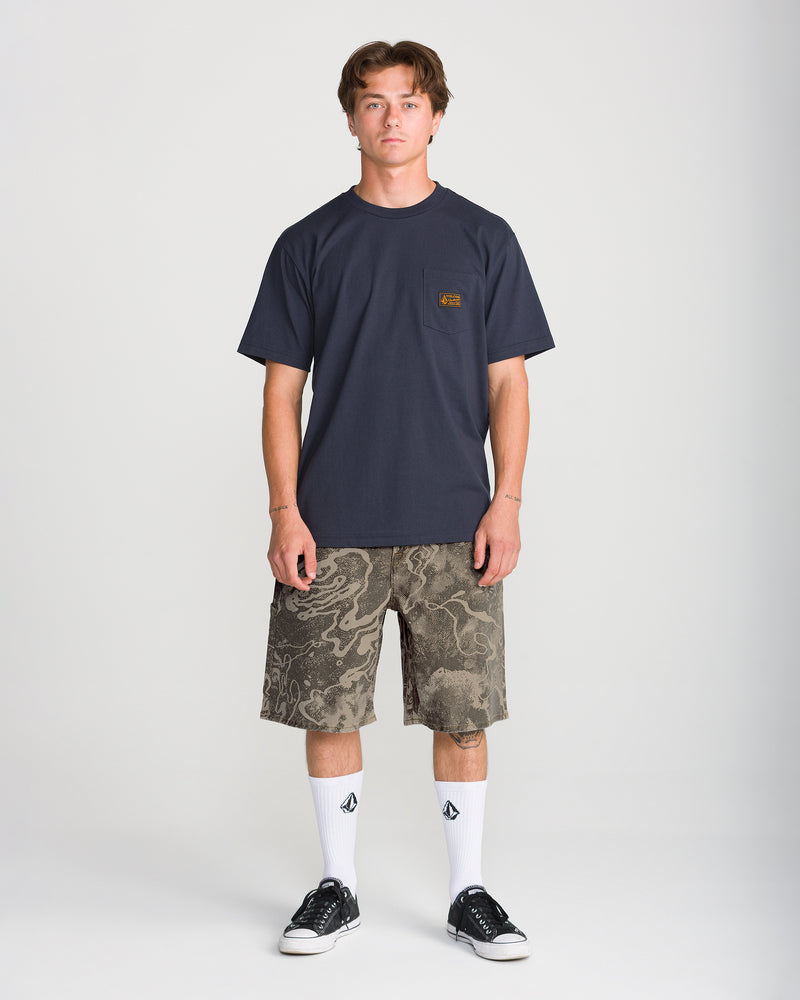 A man wearing a dark navy pocket t-shirt, Men’s Kinkade Utility Denim Short 22 in olive green, white crew socks, and black sneakers.