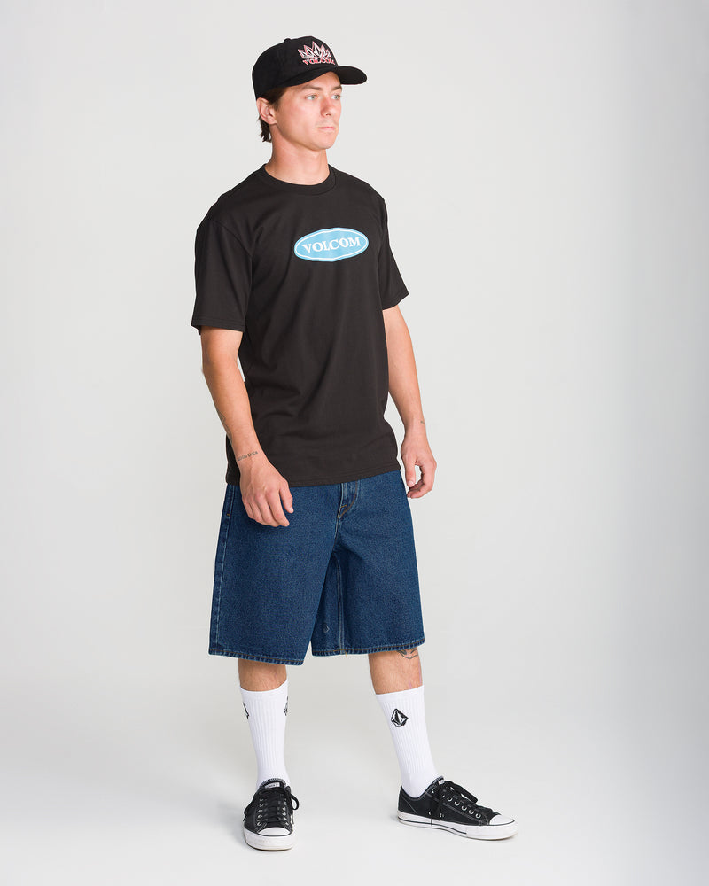 A person wearing a black t-shirt, Volcom Men’s Billow Denim Short 22 in indigo, white crew socks, and black sneakers.